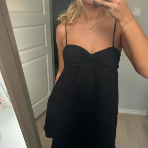 Svart kort klänning med knytband från asos - Supersöt svart kort klänning med tunna axelband som knyts på axlarna och en snygg twistad detalj vid bysten. Klänningen har en luftig passform och är perfekt för varma dagar. Materialet känns lätt och bekvämt mot huden. Från asos i storlek s💕