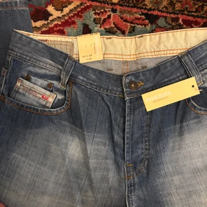 Blå jeans från Diesel - Snygga blå jeans från Diesel med klassisk femficksdesign och coola slitningar. Jeansen har orangea kontrastsömmar och en liten Diesel-logga på myntfickan. Tillverkade i Italien och i ett mjukt denimtyg som sitter skönt hela dagen.