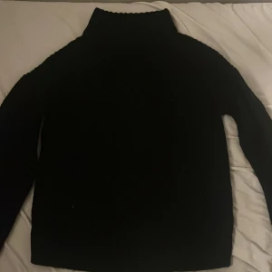 Svart polotröja från VILA - En svart polotröja från VILA i storlek S. Tröjan är stickad med hög krage och har långa ärmar. Perfekt för kyligare dagar och enkel att matcha med olika outfits.