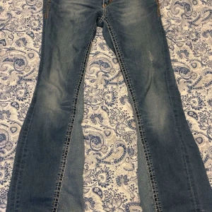 Lågmidjade bootcut jeans blå - Snygga blå jeans med låg midja och bootcut-ben. Jeansen har klassiska fickor med dekorativa sömmar och knappar bak, samt slitningar framtill för en cool look. Perfekta för dig som gillar en avslappnad och trendig stil.