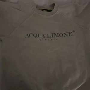 Beige sweatshirt från Acqua Limone - Beige sweatshirt från Acqua Limone med klassisk logga framtill och stor gul citron-tryck på ryggen. Storleken är 14 år men passar mig som har xs/s