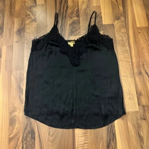 Svart linnetopp med spets från H&M - Svart linnetopp från H&M med tunna axelband och v-ringning dekorerad med snygg spets. Toppens material är glansigt och lätt. Storleken är även 40 men skulle säga att den passar en S också Perfekt att styla med jeans eller kjol. Banden går även att reglera!!🥰