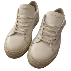 Vita sneakers från Sneaky Steve.  EST.  2007 - Säljer ett par klassiska vita sneakers från Sneaky Steve. Skorna har rund tå, platt sula och snörning framtill. Tillverkade i slätt skinn med diskret logga på plösen. Perfekta för dig som gillar en clean och stilren look.