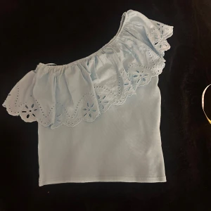 Ljusblå oneshoulder topp från Zara - Supersöt ljusblå topp från Zara med oneshoulder-design och bred volang med broderade blommor. Toppen är ärmlös och har en mjuk, ribbad känsla i materialet. Största storleken på barn men skulle säga passar xs/s. Osäker på priset så det kan definitivt diskuteras!!🥰