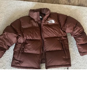 The North Face brun pufferjacka L - Brun pufferjacka från North Face i modellen W 1996 RTRO NPTS JKT, använt max 2 ggr tyvärr så därför säljer jag den. storlek L men känns mer som en M. nypris 3700, säljer för 3000, kan gå ner i pris vid snabb affär, men inte under 2500 