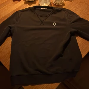 Marin blå sweatshirt från Morris - Marin blå  sweatshirt från Morris med rund halsringning och broderad logga på bröstet. Tröjan har ribbade muddar och klassisk passform, perfekt för en stilren och enkel look. Materialet är mjukt och bekvämt, passar till många tillfällen.