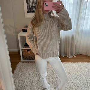 Beige ribbad stickad polotröja - Säljer en beige ribbad polotröja i stickat material. Tröjan har hög krage, lång ärm och en loose fit som ger en chill vibe. Perfekt för lager på lager under höst och vinter. Snygg att styla med både jeans och kjol.