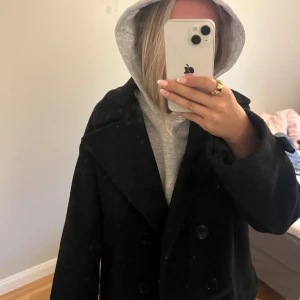 Svart skepparkavaj från DesignSi - Klassisk svart skepparkavaj från DesignSi med bred krage och dubbelknäppning framtill. Jackan har en rak passform och är fodrad för extra komfort. Perfekt för dig som vill ha en stilren och tidlös look under höst och vinter.