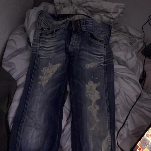 Blå bootcut jeans med slitningar - Säljer ett par blå bootcut jeans med tydliga slitningar och ljusa detaljer framtill. Jeansen har låg midja och klassisk femficksdesign. Materialet är denim och passformen är loose med bredare ben nertill. Perfekta för en avslappnad och trendig look. #stockholmstil #lowrise 