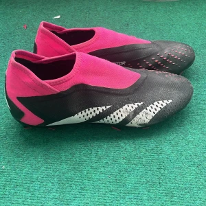 Adidas Predator rosa/svarta fotbollsskor - Säljer ett par Adidas Predator fotbollsskor i svart och rosa med vita detaljer. Skorna har en strumpliknande passform utan snöre. 
