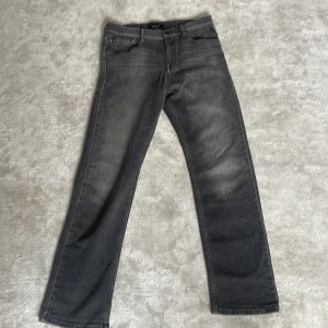 Replay grå jeans straight fit - Snygga grå jeans från Replay med klassisk femficksdesign och raka ben. Jeansen har en tvättad look med subtila slitningar och svarta detaljer på knappen. Perfekta för dig som gillar en stilren och avslappnad vibe.