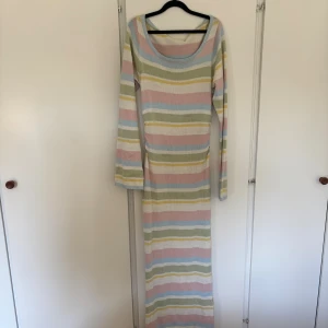 Pastellrandig långklänning - Säljer en långklänning med mjuka pastellfärgade ränder i blått, rosa, gult, grönt och vitt. Klänningen har lång ärm och rundad halsringning. Materialet är stickat och känns skönt mot huden, perfekt för dig som gillar färg och bekvämlighet. Liten maska mitt på magen, men inget som syns vid användning 