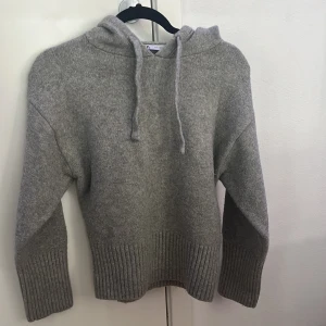 Grå stickad hoodie från Zara - Mysig grå hoodie från Zara i stickad material med huva och snörning. Tröjan har långa ärmar och breda ribbade muddar vid ärmslut och nederkant. Perfekt för chill dagar och när du vill ha det extra comfy. 
