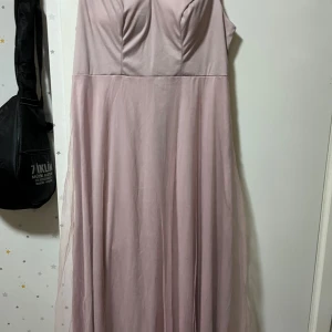 Ljusrosa långklänning med v-ringning - Säljer en elegant ljusrosa långklänning med v-ringad överdel och lätt utsvängd kjol. Klänningen är ärmlös och har dragkedja i ryggen. Materialet är tunt och ger ett flowy intryck, perfekt för speciella tillfällen. OBS DEN ÄR FRÅN SHEIN 