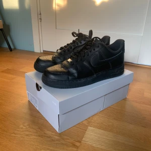Svarta Nike Air Force 1 sneakers 45,5 - Säljer ett par helsvarta Nike Air Force 1 sneakers i storlek 45,5 Skorna har snörning, rund tå och är tillverkade i skinn. Perfekta för dig som gillar en stilren och tidlös look. Levereras i originalkartong. Skriv vid minsta fundering!