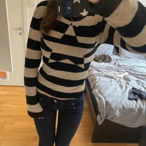 Randig stickad tröja med stjärna - Snygg stickad tröja med breda svarta och beige ränder och en stor svart stjärna på bröstet. Tröjan har lång ärm och en tight passform, perfekt för dig som gillar en cool och unik look. Är insydd till storlek xs och är i bra mattial  därav priset tror 100% ull men kan kolla om de är viktigt för dig🥰