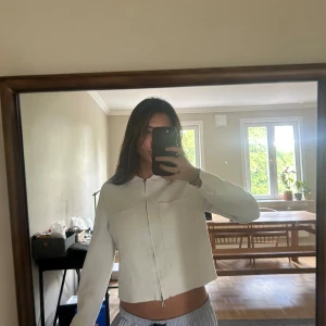 Vit croppad overshirt från Åhléns - Säljer en vit croppad overshirt från Åhléns med klassisk krage, två stora bröstfickor och dragkedja framtill. Jackan har lång ärm och är gjord i ett mjukt bomullsmaterial. Perfekt för dig som gillar stilrena och enkla plagg.