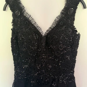 Svart långklänning med paljetter - Elegant svart långklänning med djup v-ringning och detaljerad broderad överdel täckt av paljetter och pärlor. Kjolen har flera lager volanger i tunn mesh. Endast använd en kväll. Storlek Xs men passar även S. 