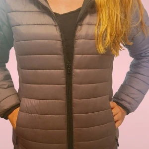 Grå pufferjacka från Dobsom - Säljer en grå pufferjacka från Dobsom med horisontella sömmar och hel dragkedja framtill. Jackan har två fickor med dragkedja och en snygg, enkel design som passar perfekt till kyliga dagar. Materialet är lätt och syntetiskt för extra komfort.