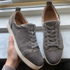 Christian Louboutin - Snygga gråa sneakers från Christian Louboutin med klassisk röd sula och signatur på undersidan. Skorna är använda men det funkar bra och man kan tvätta dem så det ser snyggare ut! STORLEK 43! Christian Louboutin märket i sulan har slitits bort när dem har blivit använda!