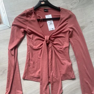 Dusty rose knytblus från Gina Tricot - Supersnygg dusty rose långärmad topp från Gina Tricot med knyt framtill och djup v-ringning. Toppens smickrande passform och långa knytband ger en trendig look. Perfekt att styla med jeans eller kjol för en cool vibe. Köpte för två år sen har inte använt den nån gång 😊
