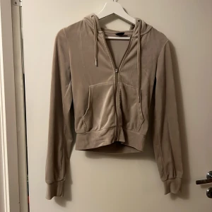 Beige velour hoodie från Gina Tricot - Supermjuk beige hoodie i velour från Gina Tricot. Tröjan har dragkedja framtill, snörning i huvan och stora fickor. Långärmad och croppad modell som ger en snygg och avslappnad look. Perfekt för chill dagar eller när du vill vara extra comfy. använd några gånger men inte blivit nopprig eller förstöd 