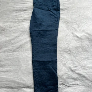 Mörkblå kostym linnebyxor med smal passform - Snygga mörkblå kostym linnebyxor med smal passform. Perfekta för dig som gillar en stilren look och vill ha något lätt och luftigt. Byxorna har en klassisk design utan synliga detaljer och passar till många olika outfits.