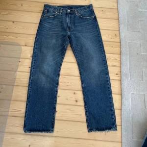 Levi's 551 Z blå jeans straight fit OANVÄNDA  - Levi's 551 Z jeans i blå denim med rak passform och normal midja. Jeansen har slitna, fransiga benslut för en cool vintagekänsla. Perfekta för dig som gillar tidlös stil och vill ha ett par jeans som funkar till allt.