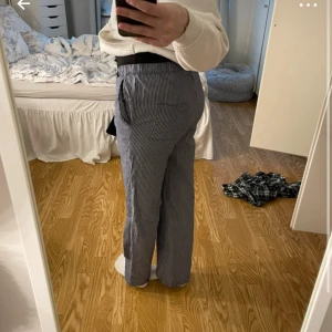Randiga byxor med snörning - Snygga byxor med smala svarta och vita ränder, elastisk midja och snörning framtill. Modellen är rak och lite loose, med fickor på sidorna. 