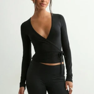 Svart omlottopp med knyt och v-ringning - Säljer en svart omlottopp med lång ärm och djup v-ringning. Toppen har knyt i sidan och är croppad vilket ger en snygg siluett. Funkar också så bra med ett linne under🤍