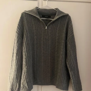 Grå stickad tröja - Mysig grå stickad tröja från Vero Moda med half zip-dragkedja och hög krage. Tröjan har ett snyggt kabelstickat mönster och långa ärmar. Endast använd någon gång, säljer då den inte kommer till användning💕