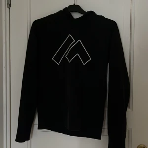 Svart hoodie  - Svart hoodie med stor vit logga på bröstet. Tröjan har huva och långa ärmar, perfekt för en avslappnad och sportig stil. Tillverkad i mjukt material som känns skönt mot huden.