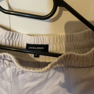 Vita mjukisbyxor från Jack & Jones - Vita mjukisbyxor från Jack & Jones med elastisk midja och snörning. Byxorna har en avslappnad passform och är tillverkade i mjukt bomullsmaterial. Liten logga på ena benet ger en clean look. Perfekta för chill dagar eller när du vill vara bekväm.