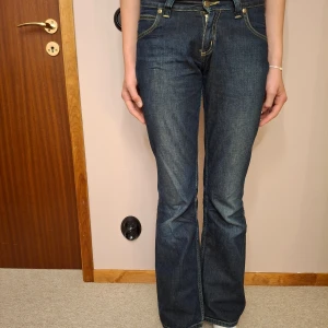 Lee bootcut jeans mörkblå - Mörkblå jeans från Lee med bootcut passform och klassiska gula sömmar. Byxorna har fem fickor. Perfekta för dig som gillar en tidlös jeansstil.