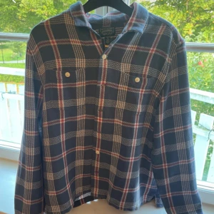 Rutig henley från Polo Ralph Lauren - Säljer en blå och röd rutig henley från Polo Ralph Lauren Polo Country. Skjortan har långa ärmar, två bröstfickor med knappar och klassisk krage. Tillverkad i mjuk bomull, perfekt för en chill och avslappnad stil.