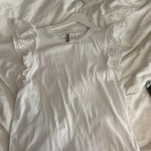 Vit blus med spetsärmar från Soyaconcept - Supersöt vit blus från Soyaconcept i storlek XS. Toppen har rund hals och ärmlös design med breda, volangiga spetsärmar som har broderade detaljer. 