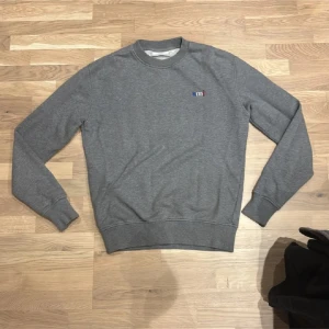 Grå sweatshirt från Ami Paris - Snygg grå sweatshirt från Ami Paris med diskret broderad logga på bröstet. Tröjan har rund hals, ribbade muddar och är tillverkad i mjuk bomull. Perfekt för dig som gillar stilrena och klassiska plagg med en modern touch. Storlek XS passar dig som är ca 175-180cm lång🫵🏼                        Hör av dig för minsta lilla fundering!❤️🫵🏼