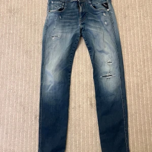 Replay Anbass blå jeans - Säljer ett par Replay Anbass jeans i blå tvätt med slitningar och hål på benen. Jeansen har fem fickor, normal passform och är tillverkade i stretchig denim. Snyggt slitna detaljer och klassisk Replay-logga på bakfickan.