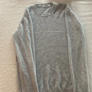 Grå kashmirtröja från J.Lindeberg - Mjuk och stilren grå tröja från J.Lindeberg i kashmir. Rund halsringning med ribbade muddar vid ärmslut och nederkant. Klassisk passform och långärmad, perfekt för dig som gillar enkel och clean look. Knappast använd 