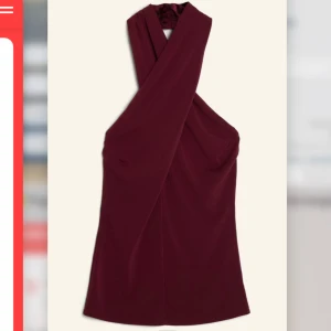 Vinröd omlott festtopp - Supersnygg vinröd festtopp med omlott-design och breda axelband som korsas framtill. Den är ärmlös och har en elegant, figurnära passform som framhäver siluetten. Perfekt för dig som vill sticka ut med en stilren look. 