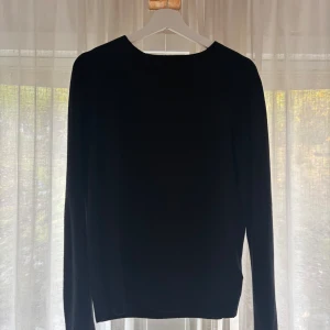 Svart långärmad stickad tröja - En klassisk svart stickad tröja med rund hals och långa ärmar. Enkel och stilren modell som passar perfekt till jeans eller kjol. Tröjan har en rak passform och är mjuk och skön att bära.