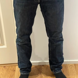 Mörkblå jeans från Nudie Jeans - Nypris: 1499 Säljer ett par mörkblå jeans från Nudie Jeans med klassisk femficksdesign och snygga kontrastsömmar. Modellen heter gritty jacksson blue slate. Jeansen har raka ben och normal passform, samt detaljerade bakfickor med Nudie Jeans signatursöm. Perfekta för en avslappnad stil. Inga tecken på slitage!