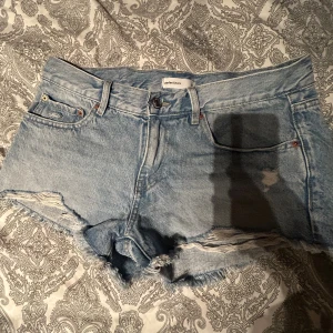 Lågmidjade jeansshorts - Säljer ett par ljusblå jeansshorts från Ginatricot med fransiga kanter och slitna detaljer framtill. Klassisk femficksmodell med bälteshällor och knappstängning. Perfekta för varma dagar och en avslappnad look.Aldrig använda‼️.                           Köpta för ca 300 kr