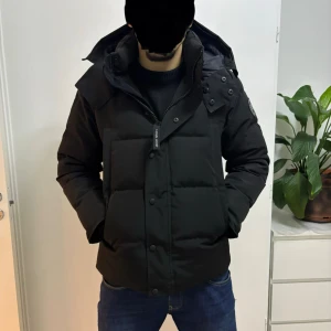 Svart dunjacka från Canada Goose - Säljer en svart dunjacka från Canada Goose blacke lable med huva och klassisk patch på ärmen. Jackan har en stilig och fin passform, stora fickor framtill och stängs med dragkedjor. Perfekt för kalla dagar och riktigt snygg till jeans.