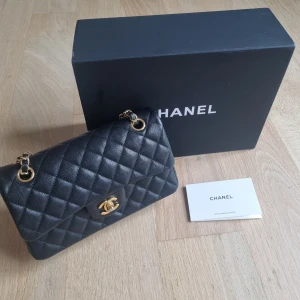 Svart quiltad axelväska - Supersnygg svart axelväska  med klassiskt quiltat mönster och guldfärgade detaljer. Väskan har en ikonisk kedjerem med logga fram i vredet. Perfekt storlek för det viktigaste och en riktig statement piece. Köpt för 7000:- helt oanvänd. 