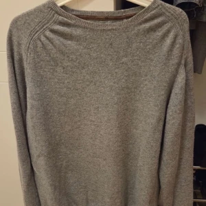 Grå stickad tröja från Massimo dutti  - En enkel och stilren grå stickad tröja med rundad hals och långa ärmar. Tröjan har ribbade detaljer vid halsringningen och axlarna, vilket ger en snygg touch. Perfekt för att hålla sig varm under kyliga dagar.