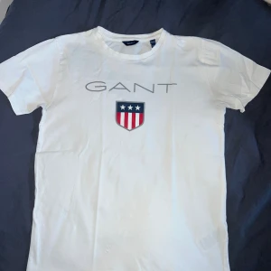 Vit GANT t-shirt  - Vit t-shirt från GANT som endast är tvättad ett par gånger. Den är i fint skick förutom några hål längst ner på plaggets framsida (se sista bilden).
