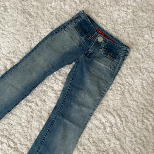 Blå bootcut jeans från Miss Sixty - Snygga blå jeans från Miss Sixty med bootcut passform och coola fickdetaljer både fram och bak. Jeansen har låg midja, slitningar och klassisk knappstängning. Perfekta för dig som gillar en retro vibe och vill sticka ut lite extra. 💞(aldrig använda av mig, köpte på selpy)  Mått:  • Midja: 32 cm  • Mellan skrevet: 18 cm • längd vid ben: 81 cm  • längst ner: 21 cm
