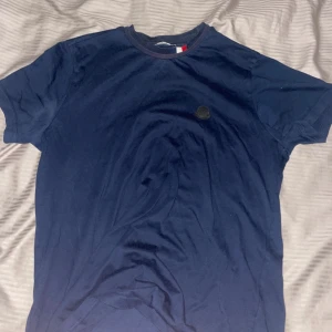 Mörkblå Moncler t-shirt i bomull - Snygg mörkblå t-shirt från Moncler med klassisk rund hals och diskret logga på bröstet. Tillverkad i mjuk bomull som känns skön mot huden. Perfekt för dig som gillar stilrena och exklusiva plagg. Röd vit detalj runt halsen. Storlek S