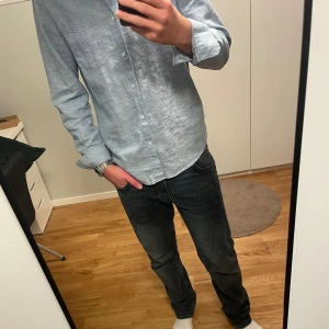 Blå linneskjorta  - Säljer en stilren ljusblå linneskjorta från Lindex i luftig linnemix. Skjortan har klassisk krage, knäppning framtill och lång ärm. Perfekt för dig som gillar en clean och enkel look.